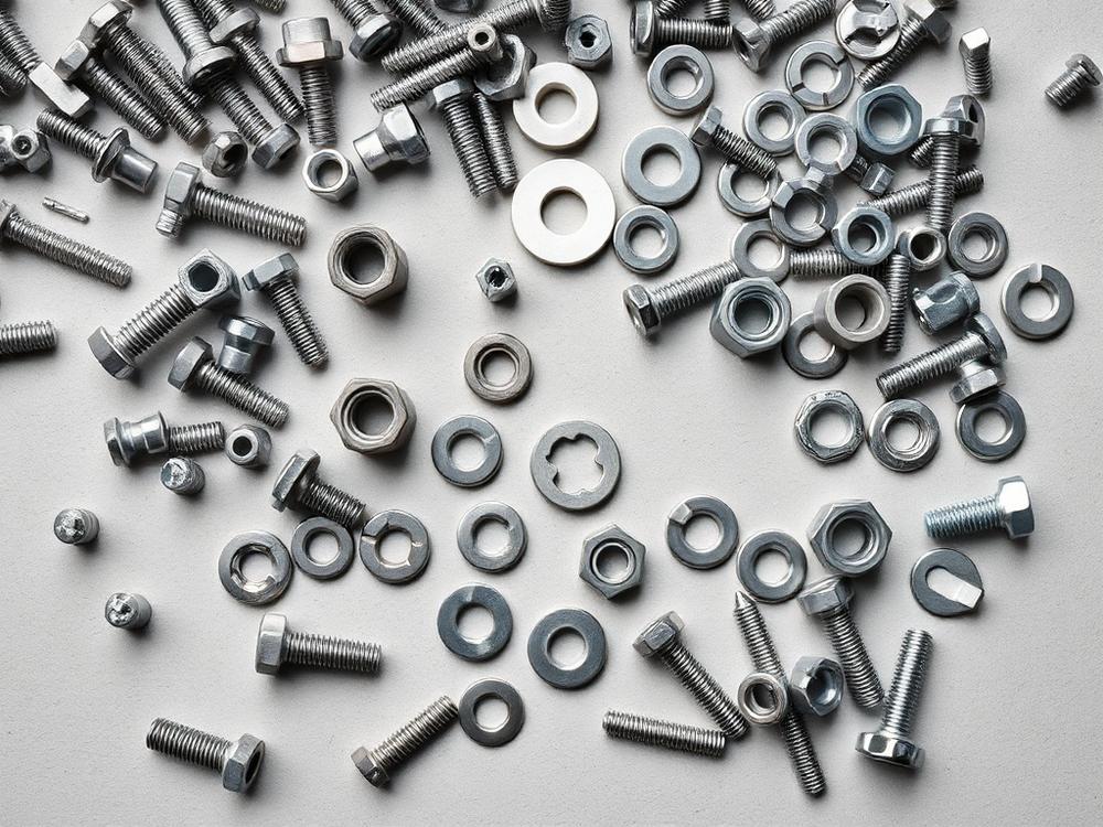Assorted steel bolts, nuts and washers arranged on a light surface